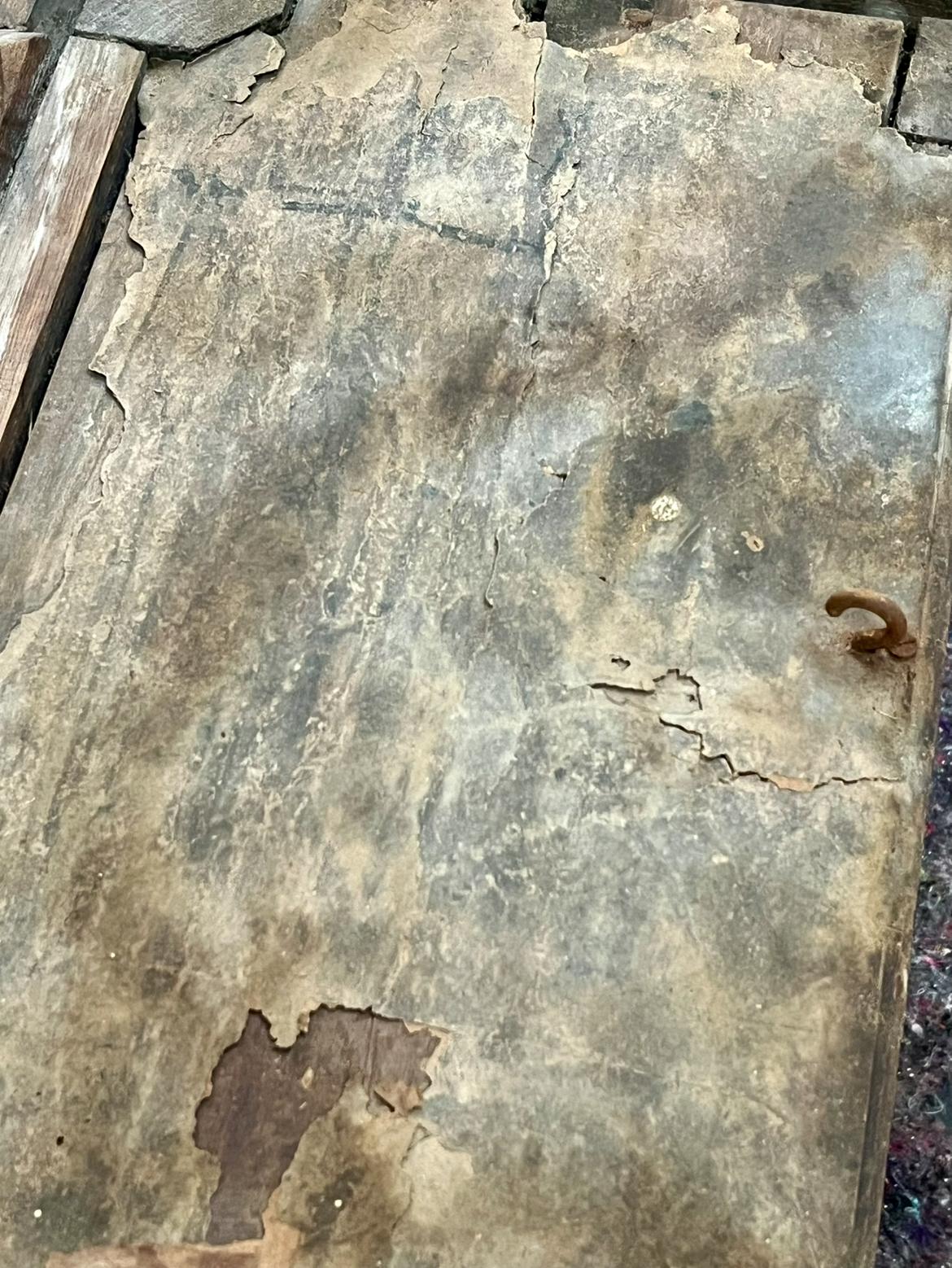 A section of the roof with a forged hook near the edge, surrounded by heavily cracked paper