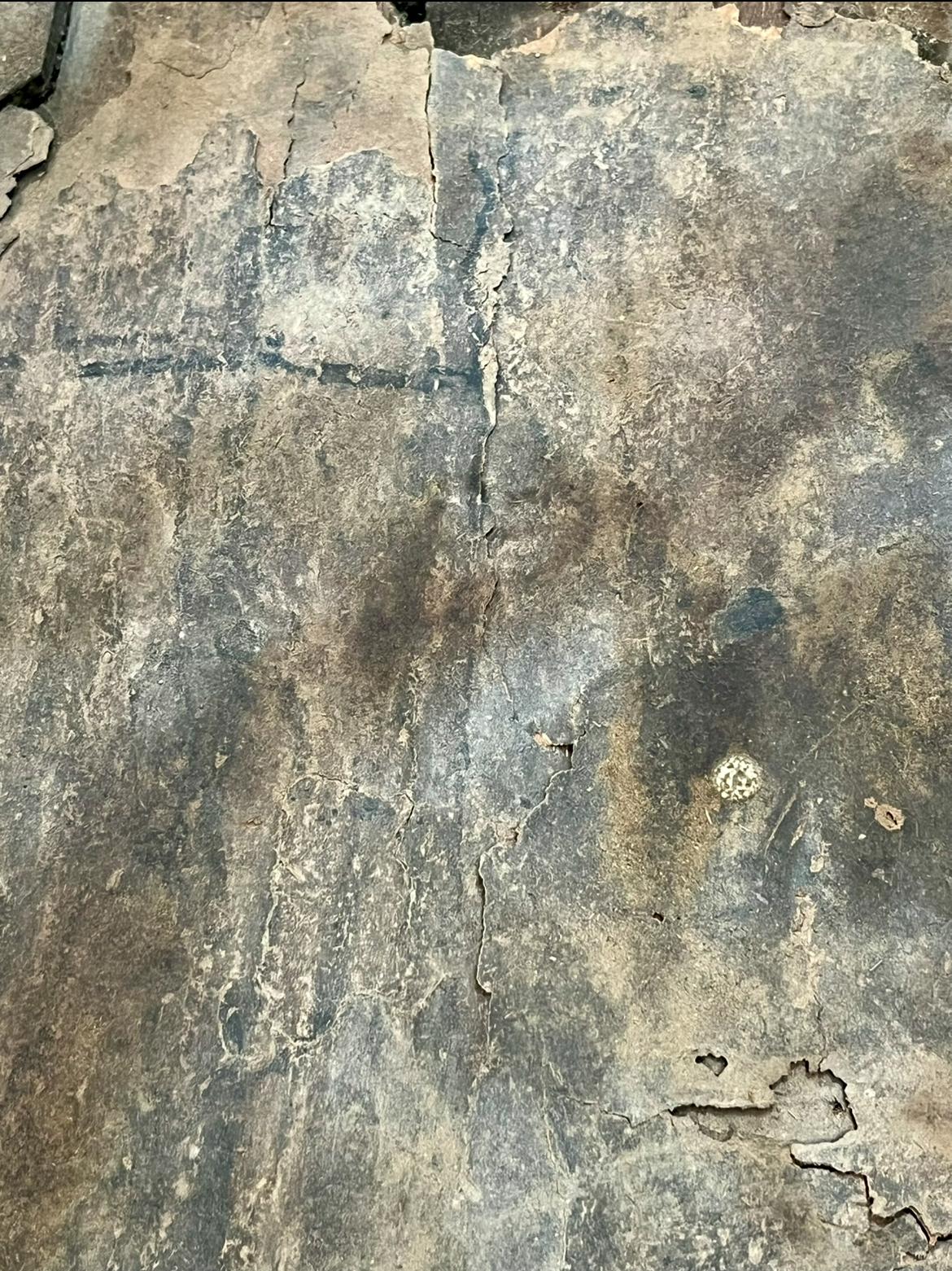 A close-up of the old layer's texture, showing stains, cracks, and a faint ruled line