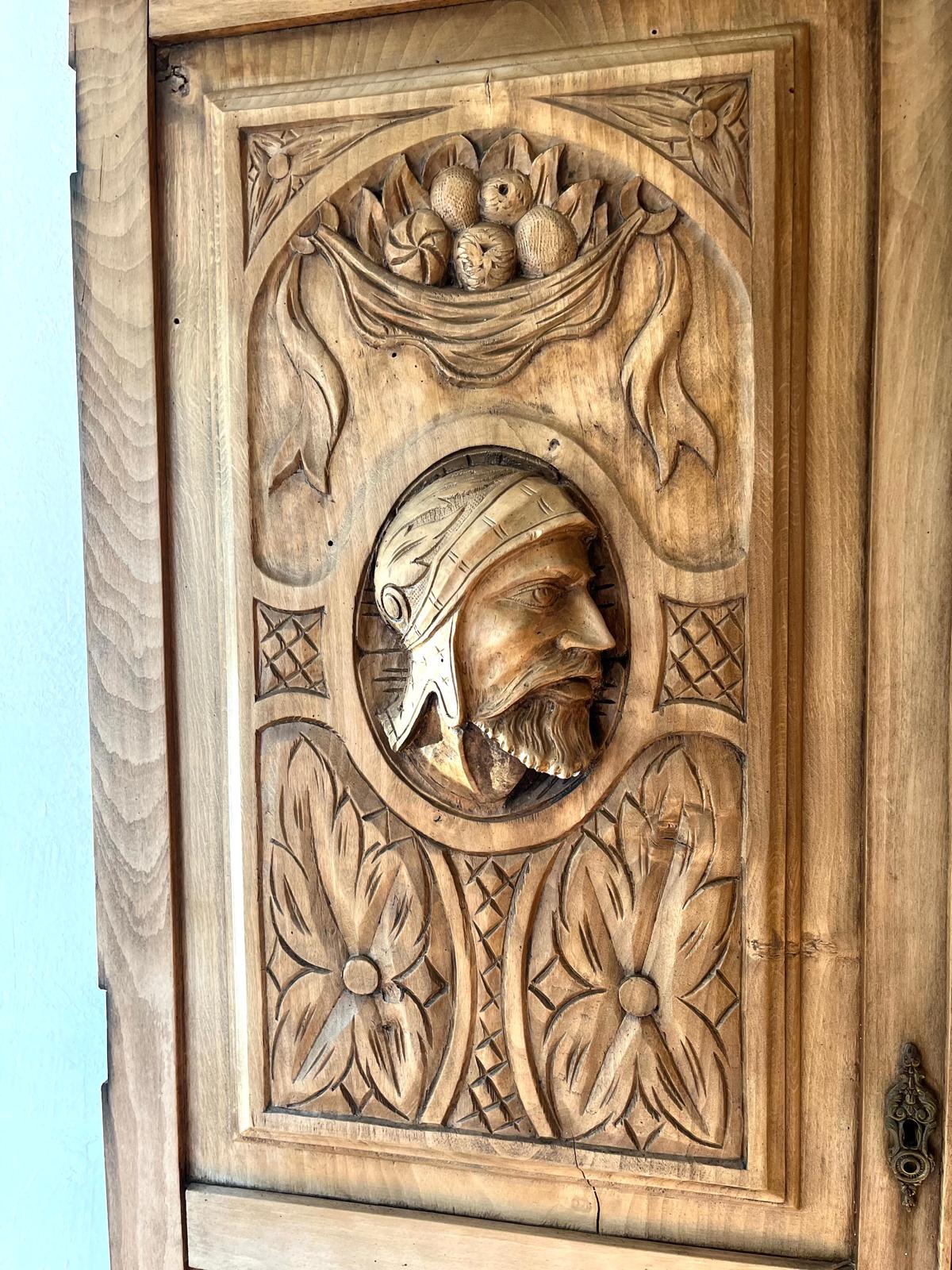 The warrior's profile in a helmet on the left panel, set within an oval medallion with a fruit garland above it