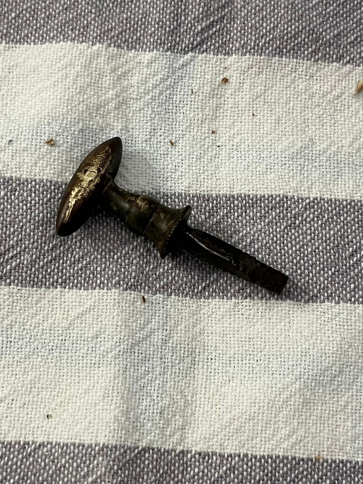 The extracted brass mushroom-handle with its forged, faceted pin, on a cloth background